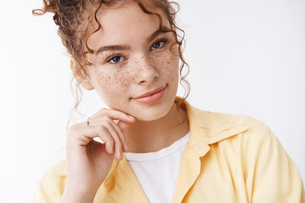 Close-up tender feminine young 20s female university student redhead freckles cheeks smiling gently touch cheek tilting head expressin sensuality, flirting standing white background