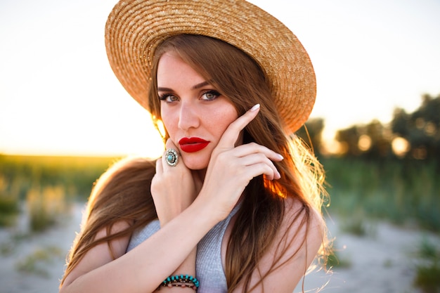 Close up tender portrait of beauty sensual woman posing on field, vintage style, wearing straw trendy hat, nature beauty make up, freckled face and red full lips.