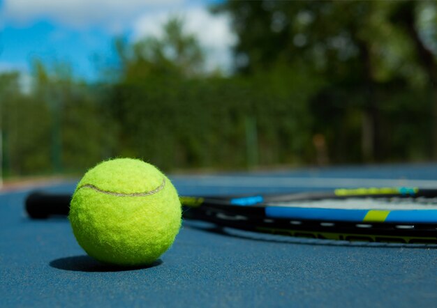 Закройте теннисный мяч на ковре профессиональной ракетки, лежа на синем ковре теннисного корта.