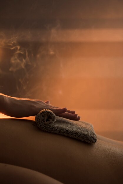 Close-up of a therapist hand massaging woman's back with hot towel in spa