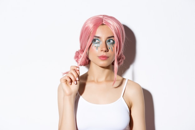 Close-up of thoughtful attractive girl with pink anime wig and bright makeup, looking at upper left corner banner and thinking, making choice, standing.