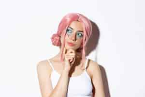 Free photo close-up of thoughtful attractive girl with pink anime wig and bright makeup, looking at upper left corner banner and thinking, making choice, standing.