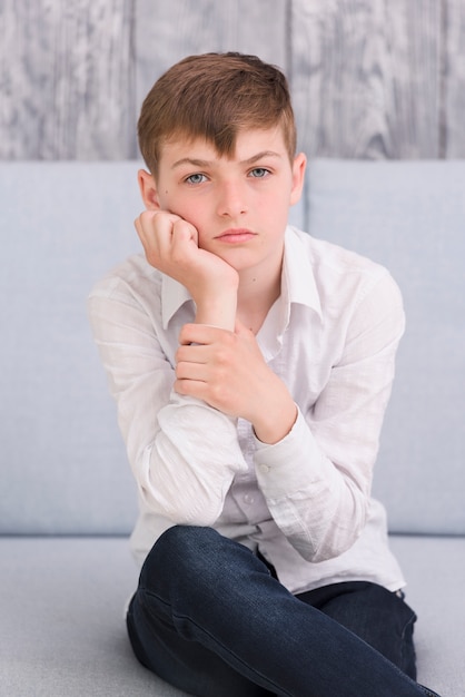 Close-up of a thoughtful boy sitting on sofa looking at camera