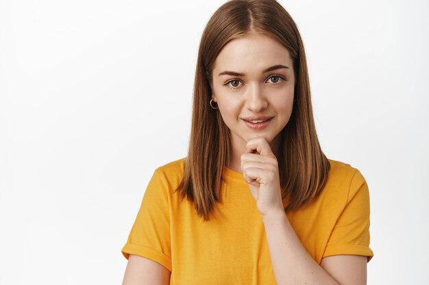 Close up of thoughtful and confident young woman, looking interested and self-assured at camera, listening to smth interesting, standing and ponder smth, white background.