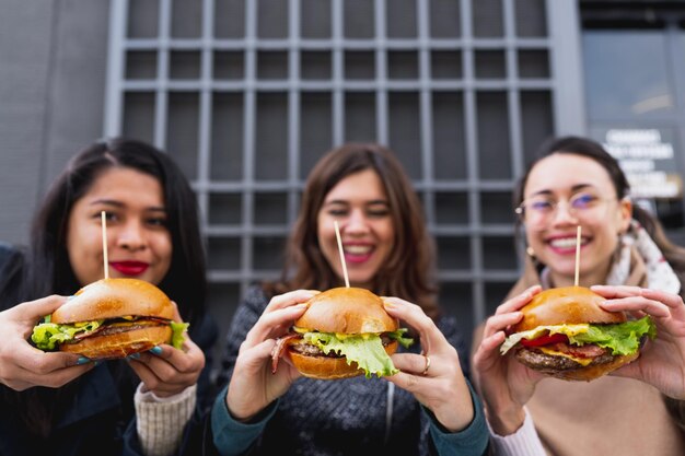 背景​の​幸せな​笑顔​の​女性​によって​保持されている​3​つ​の​ハンバーガー​の​クローズアップ​。