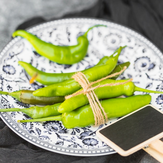 Free photo close-up of tied fresh green chili peppers and blank slate on plate