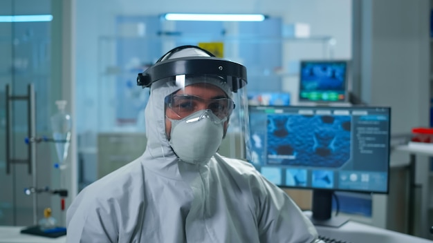 Крупным планом усталый доктор химик человек в комбинезоне, глядя на камеру, работающую в научно оборудованной лаборатории