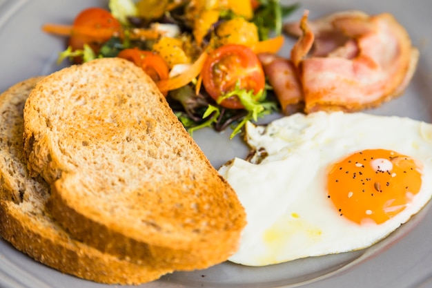 Free photo close-up of toast; fried eggs; salad and bacon on gray ceramic plate