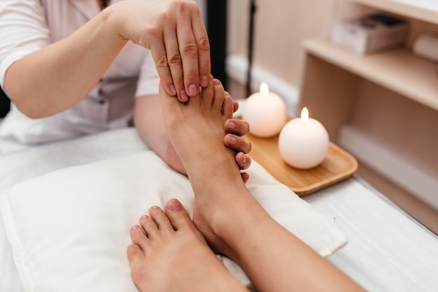 Close-up top view of male masseur massaging feet to young woman lying on massage table. professional physiotherapist with strong hands performing foot massage. concept of massage spa treatments