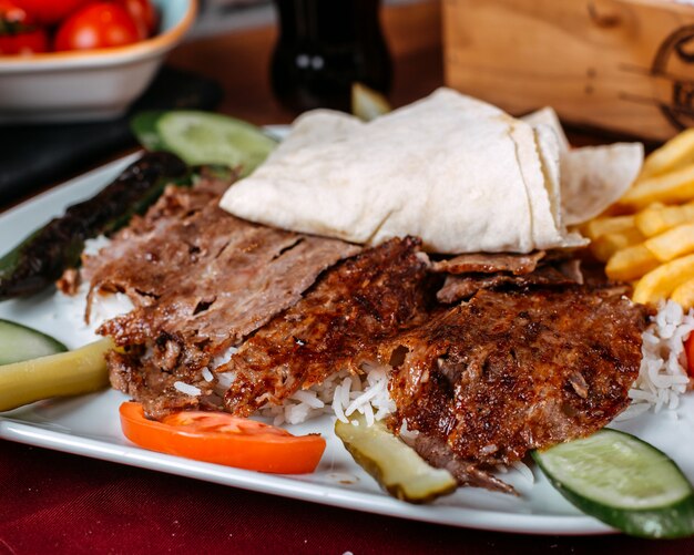 Крупный план мяса турецкого шашлыка с рисом, картофелем фри и свежими овощами на тарелке