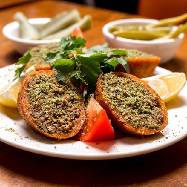 Close up of turkish stuffed meatballs ichli kofte served with lemon tomato and parsley
