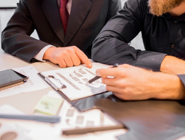 Close-up of two businessmen pointing at business chart at meeting