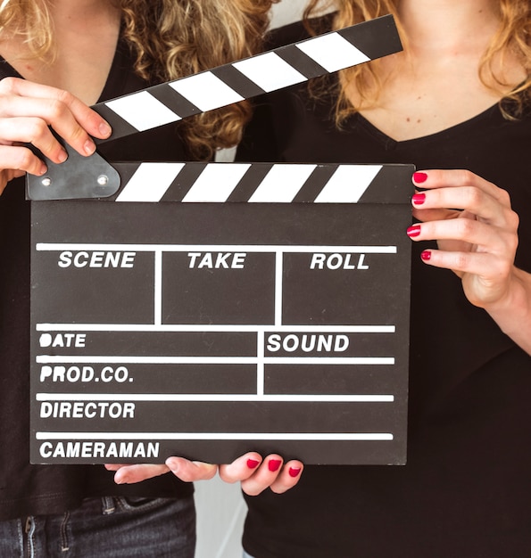 Close-up of two female friends holding clapper board