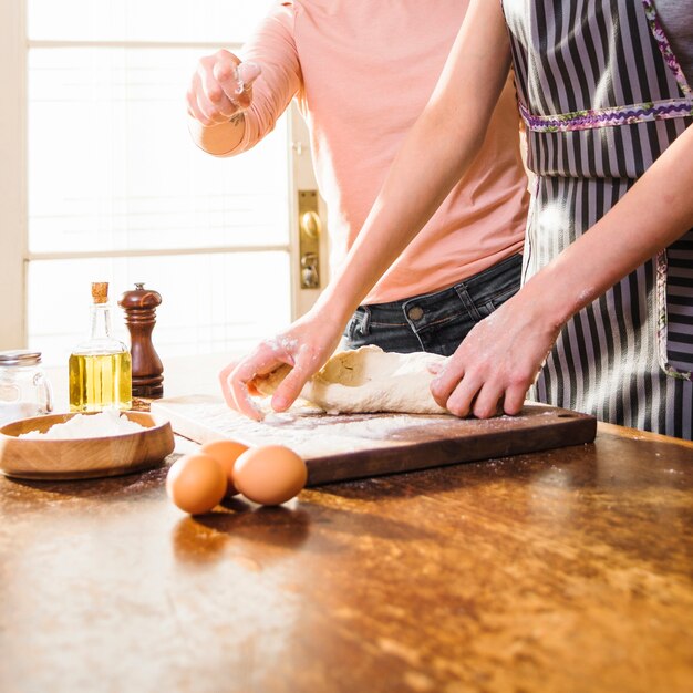 Close-up of two female friends preparing the dough on chopping board