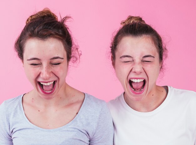 Close-up of two female friends shouting against pink background