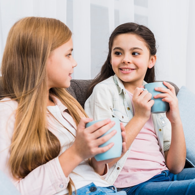 Close-up of two friends sitting on sofa looking at each other holding coffee mug in hands