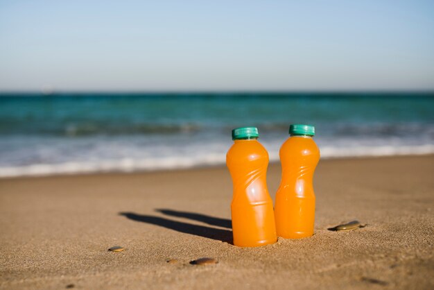 Close-up of two orange juice bottles near the seashore