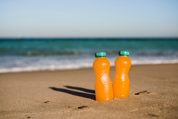 Крупный план двух бутылок апельсинового сока возле моря
