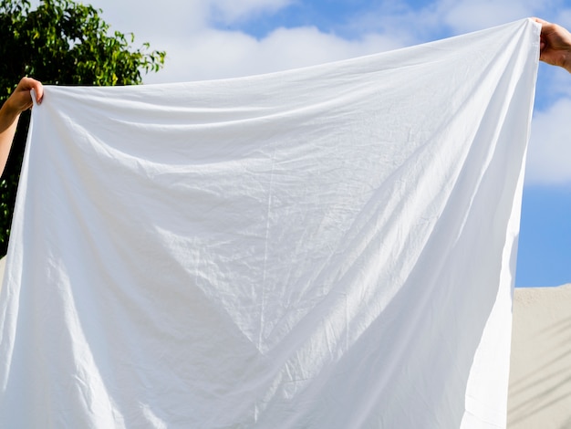 Free photo close up two people hanging a white sheet on the line