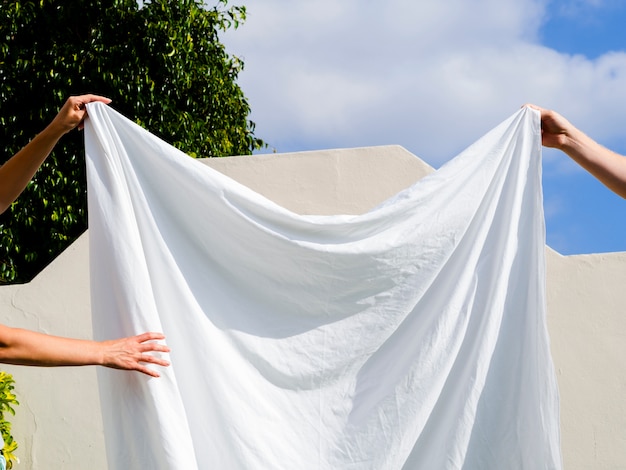 Close up two people hanging a white sheet on the line