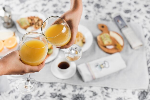 Close-up of a two people toasting juice glasses over the breakfast on table