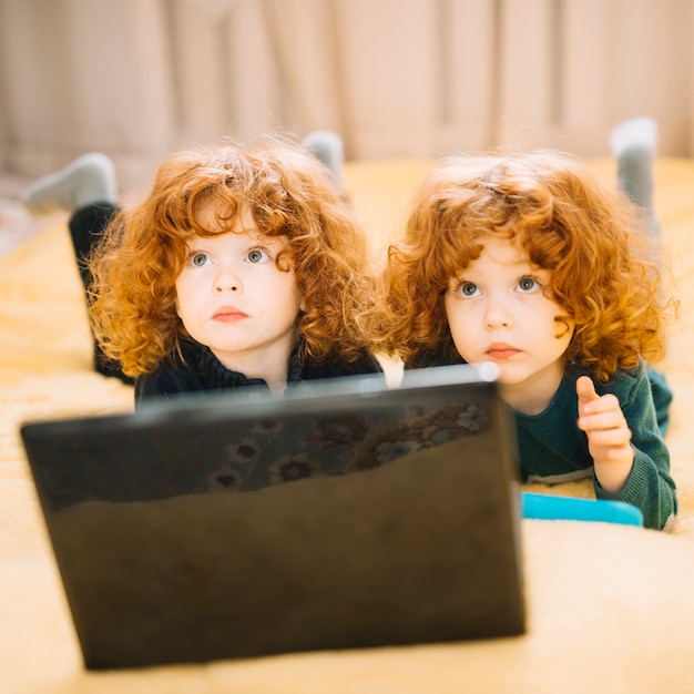 Free photo close-up of two pretty twins lying in front of laptop looking up