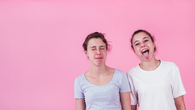 Крупный план две сестры, делая смешные лица на фоне розовый