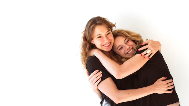 Close-up of two smiling sisters hugging each other on white background