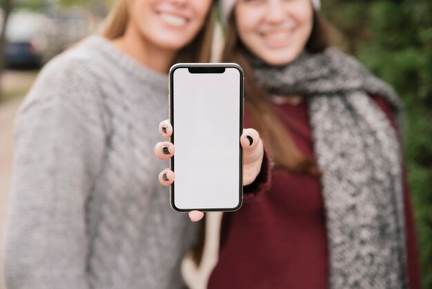 Крупным планом две улыбающиеся женщины, держа в руках телефон