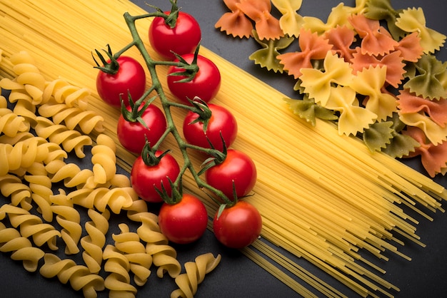 Close-up of types of uncooked pasta and fresh juicy red tomatoes