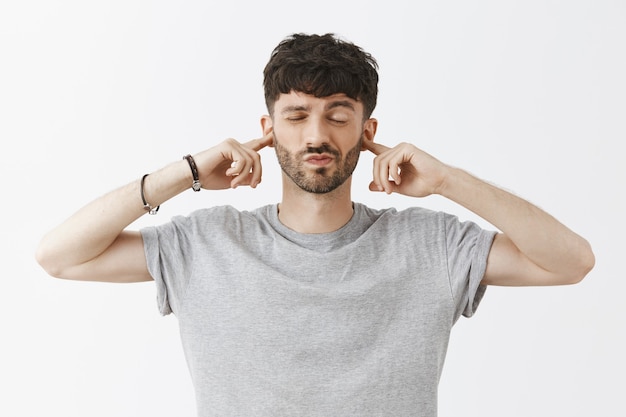 Close-up of unbothered handsome guy posing against the white wall