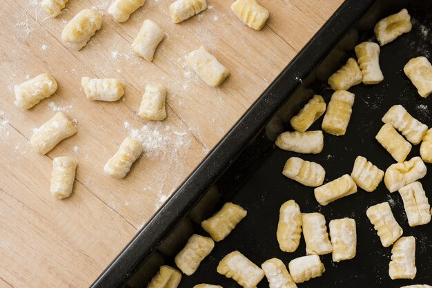 Close-up of uncooked homemade potato gnocchi pasta on baking tray and desk