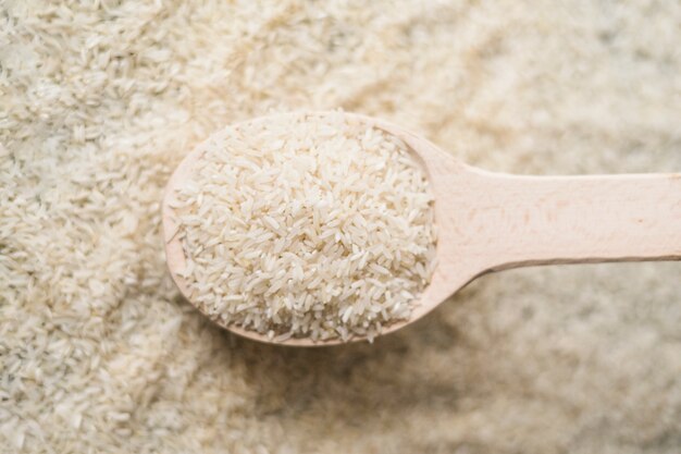 Close up uncooked rice in wooden spoon on rice background