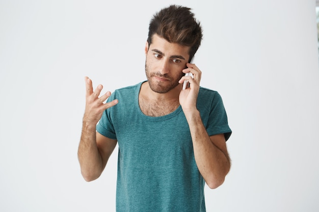 Close up of unhappy mature caucasian guy wearing blue tshirt, being pissed during argument on the phone with his mother. Negative emotions.