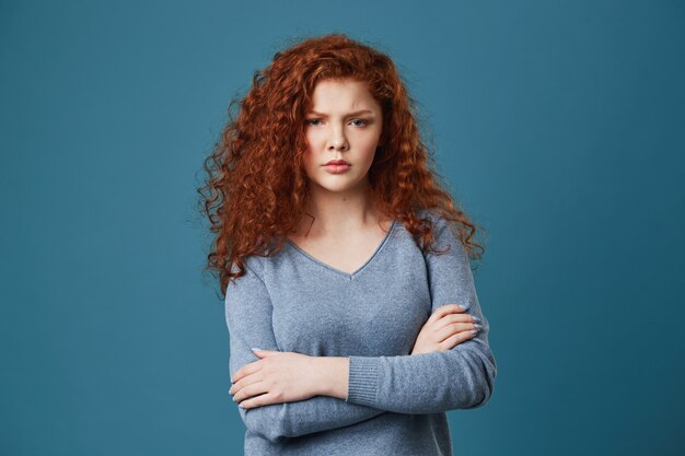 Close up of unhappy young woman with red wavy hair and freckles being angry and jealous seeing her boyfriend with other woman.