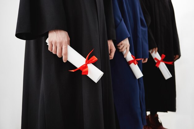 Close up of university students graduates in mantles holding diplomas.