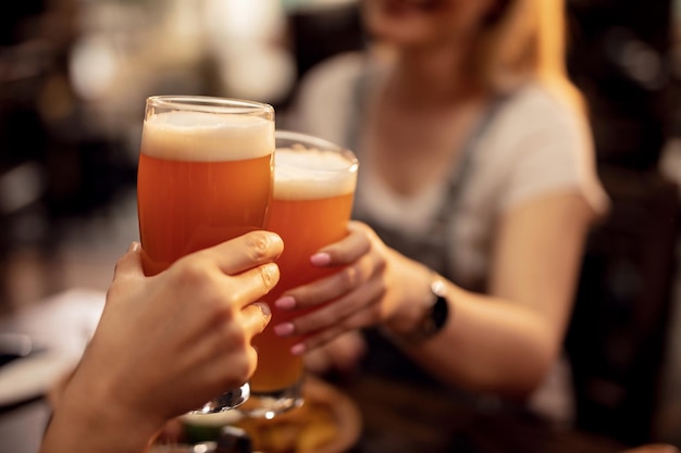 Close up of unrecognizable couple toasting with lager beer in a bar