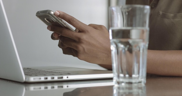 Close up video of an attractive girl's hands in an office holding a smartphone then picking up a glass of water and beginning to type on her laptop keyboard