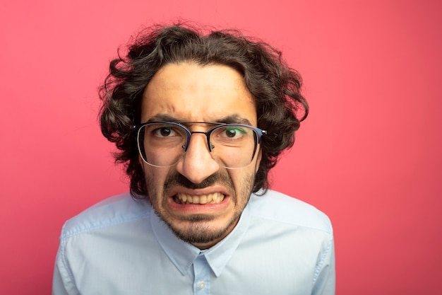 Close-up view of annoyed young handsome man wearing glasses looking at front isolated on pink wall