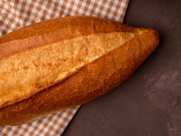 Close-up view of baguette on plaid cloth on maroon background with copy space