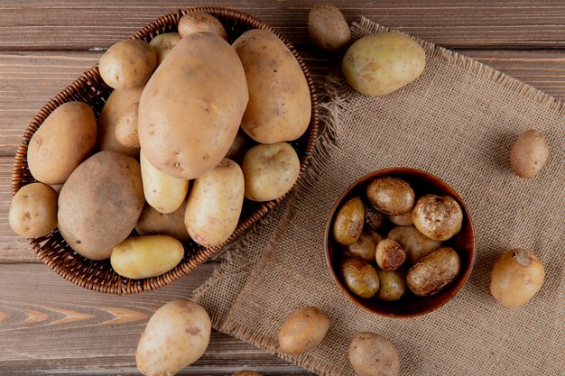 Close up view of basket and bowl full of potato on sackcloth on wooden background