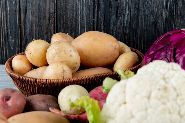 Крупным планом вид корзины, полной картофеля с другими овощами вокруг на деревянном фоне с копией пространства