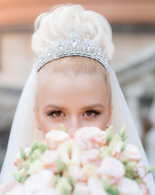 Primo piano della vista di una bellissima sposa in una preziosa corona con un bouquet tra le mani