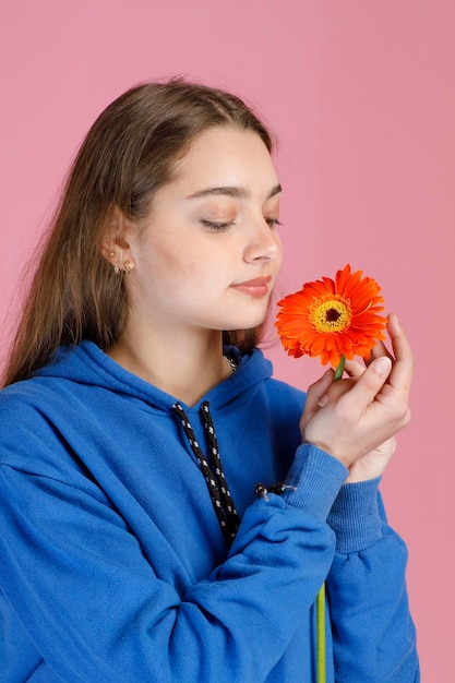 Close up view of beautiful girl admiring delicate orange gerbera flower while inhaling aroma