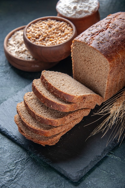 Close up view of black bread slices flour oatmeal buckwheat on dark color board on blue distressed background