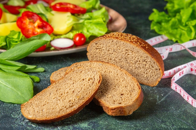 Close up view of black bread slices fresh chopped vegetables on a plate and meters green bundle on dark colors surface