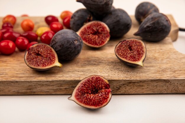 Close up view of black figs on a wooden kitchen board with cornelian cherries isolated on a white wall