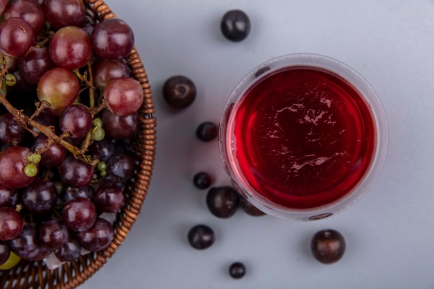Крупным планом вид сока черного винограда в стакане с виноградом в корзине и на сером фоне