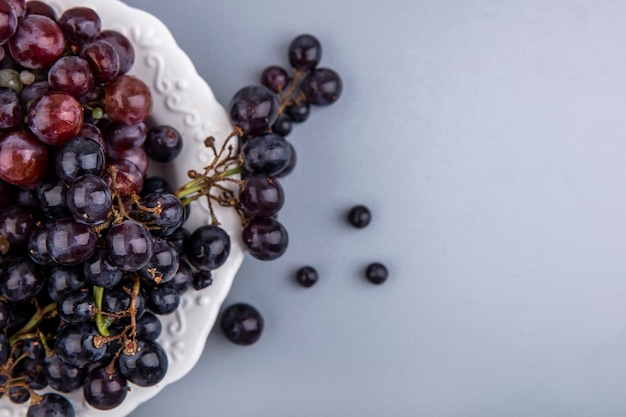 Free photo close-up view of black and red grapes in plate on gray background with copy space
