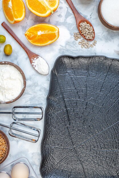 Close up view of black tray and flour in a brown bowl fresh oranges eggs sugar on ice background